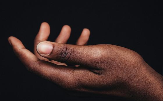 The hand of a Black person, palm up, against a black background (Unsplash/Nsey Benajah)