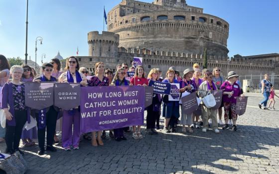 Women hold banners, in background is the Castel Sant'Angelo